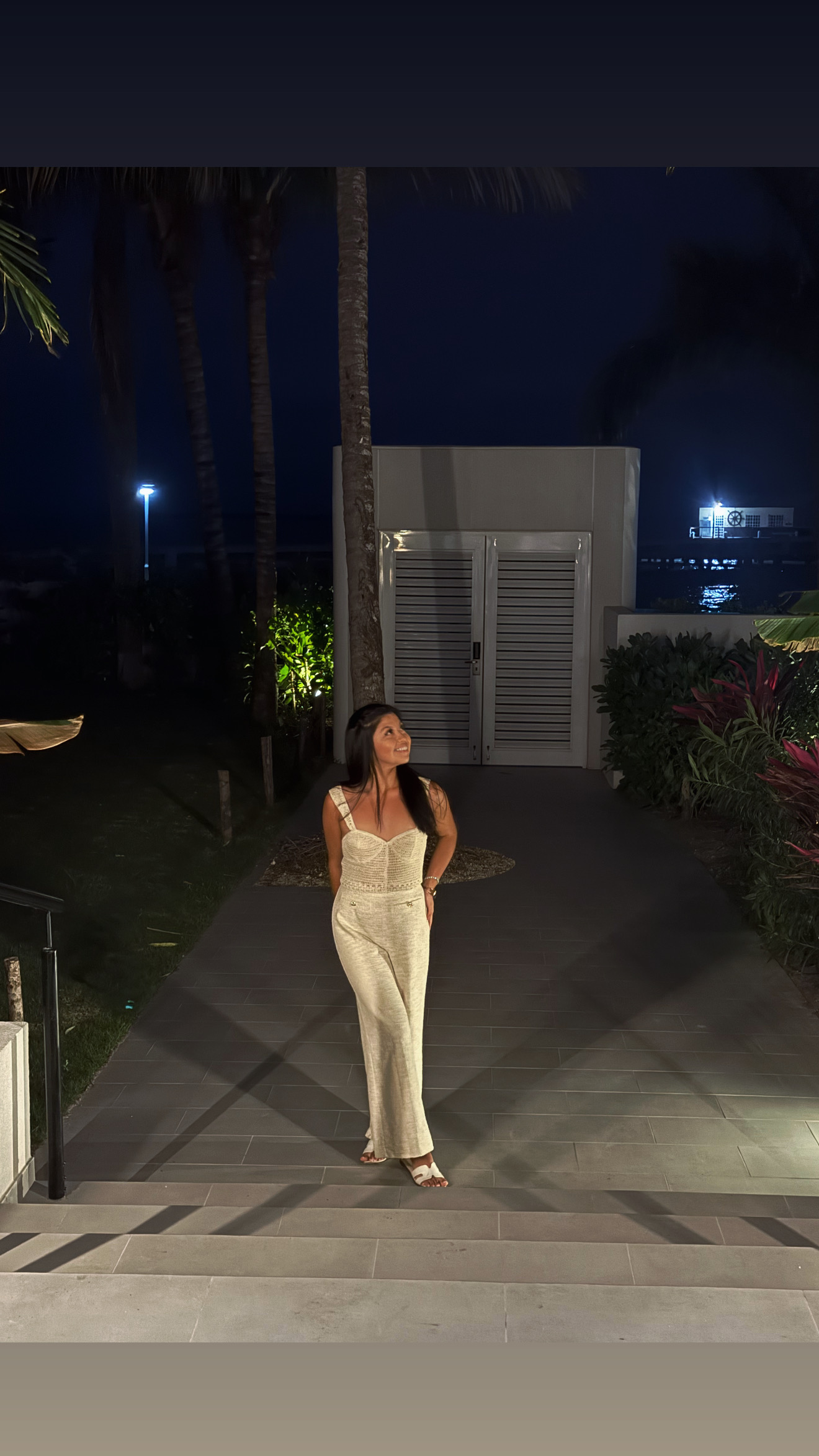 Leslee in a cream jumpsuit at night on a resort walkway